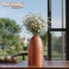 Lọ hoa gốm đặt bên cạnh cửa sổ, bên ngoài là bầ...